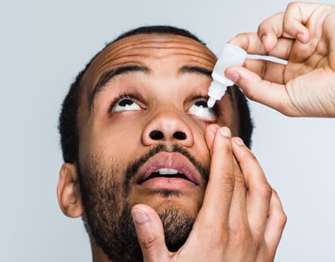 African American man using eye drops for glaucoma treatment